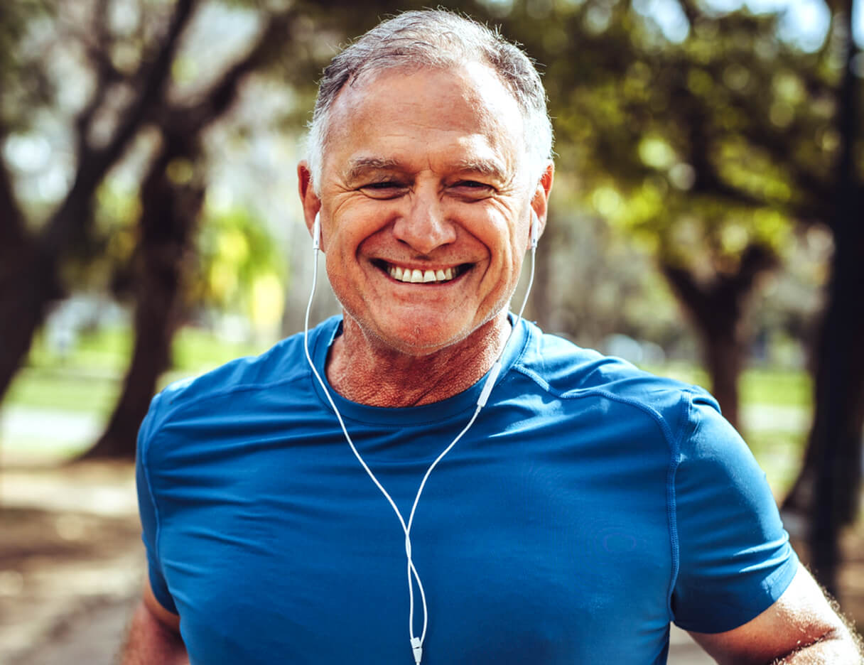 Older man smiling outdoors while listening to music