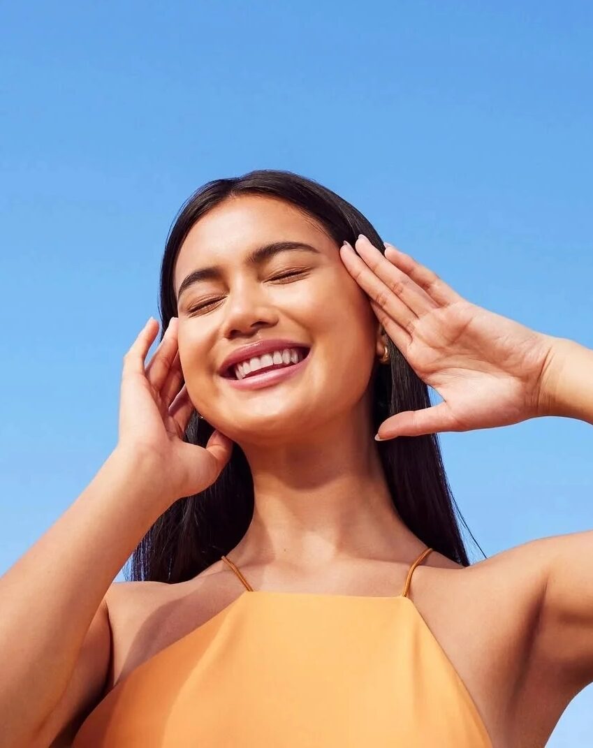 Smiling woman with glowing skin under a clear blue sky